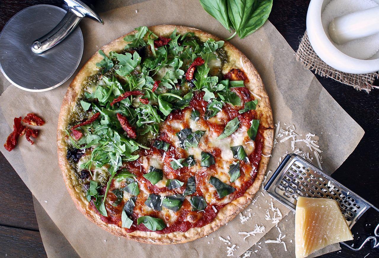 Pizza na stole jest posypywana tartym parmezanem